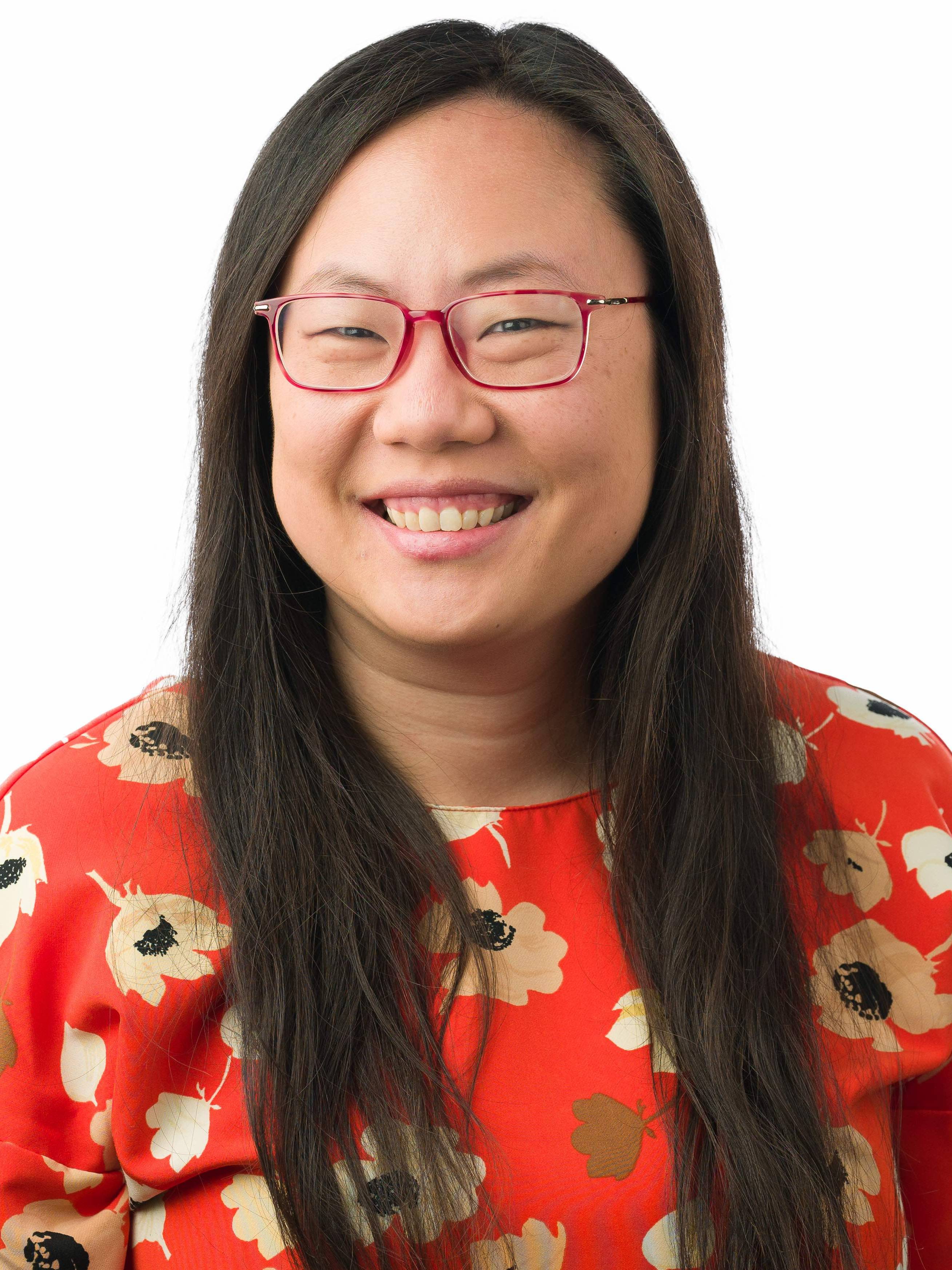 Smiling chinese woman with long brown hair wearing red framed glasses and a red blouse with big white flowers