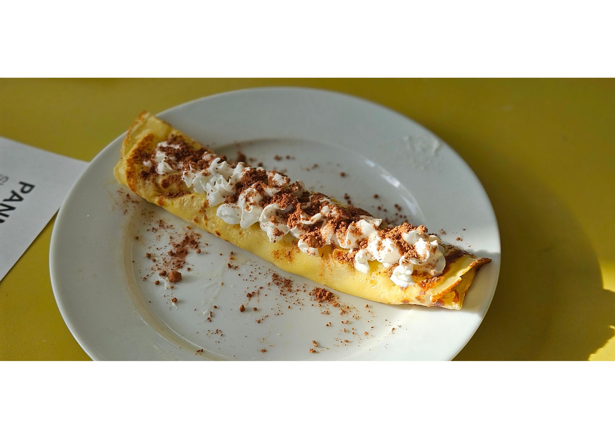 A crepe displayed on a white plate with whipped cream and cocoa sprinkled on top