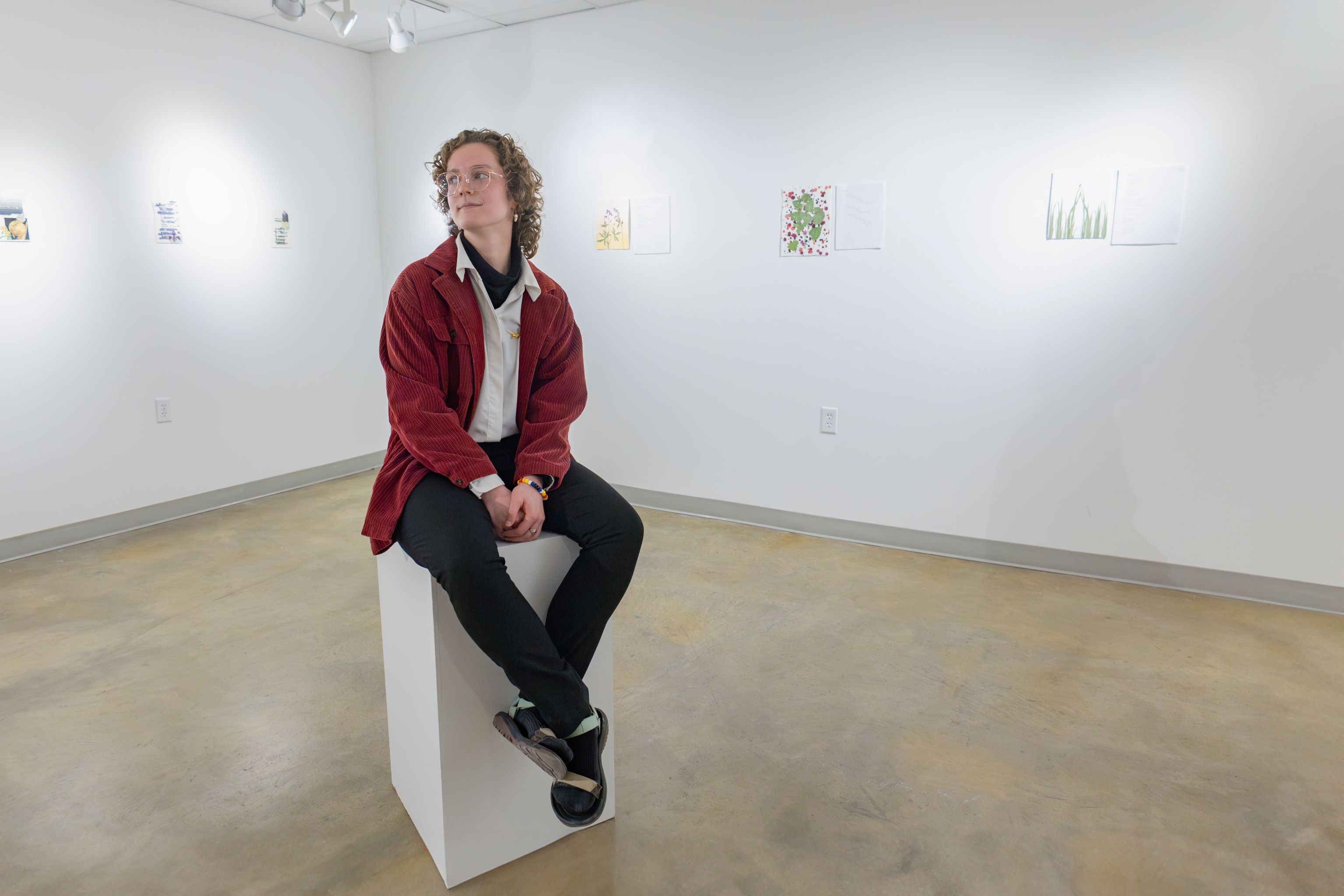 Basil Payne sitting on art stand in gallery with poetry exhibition pieces on the wall walls around them