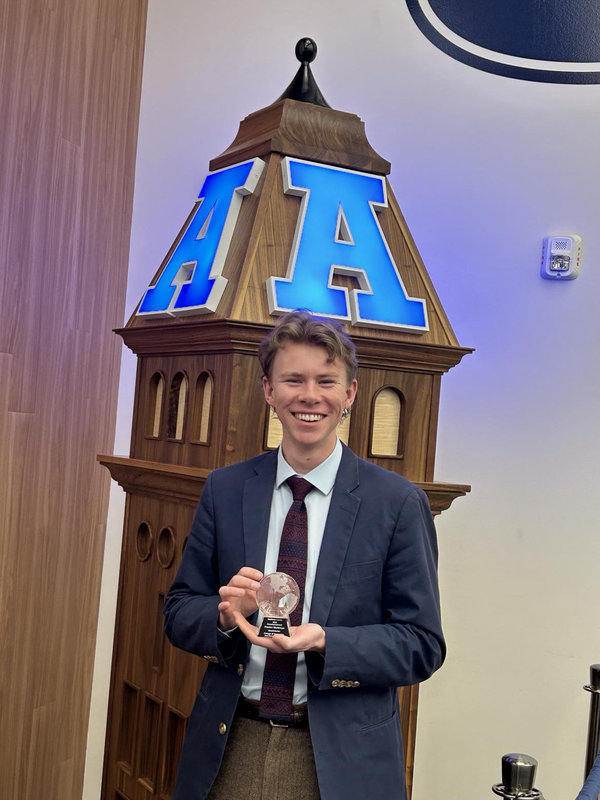 Preston Waddoups standing in front of a small Aggie A wooden stand holding valedictorian award.