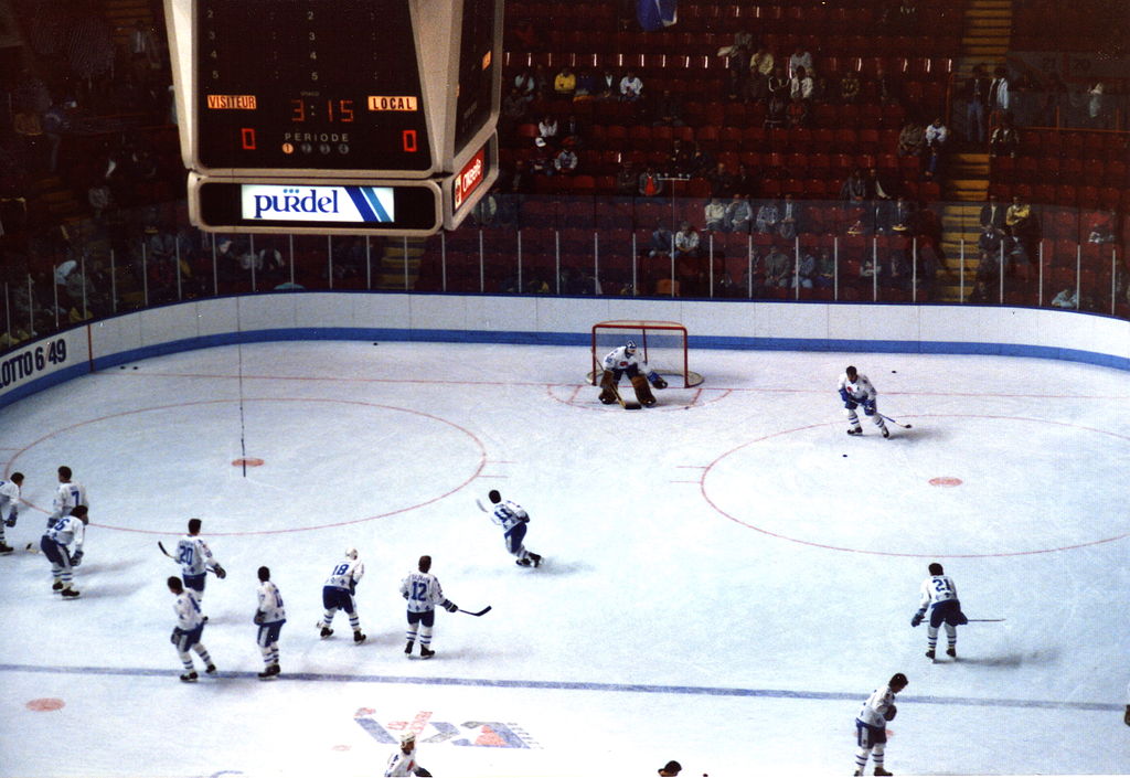 Warm-up period before a match of the Nordiques de Québec. Hockey players are scattered around the ice doing drills.