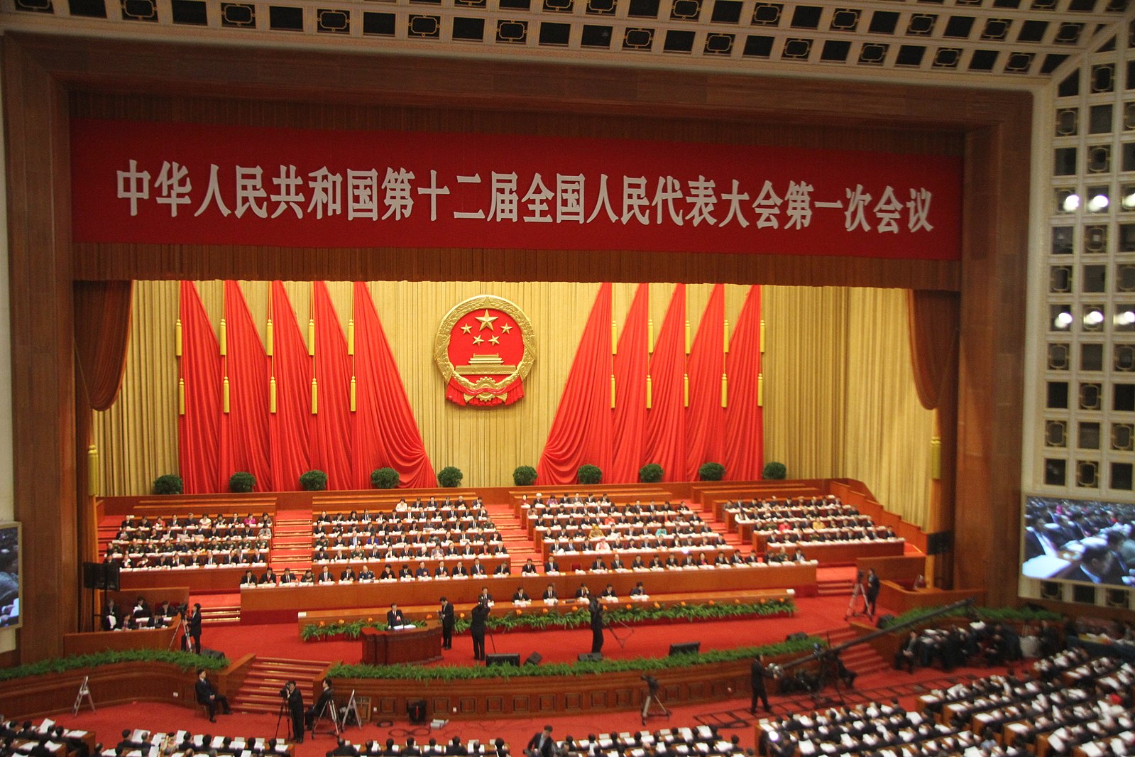 Picture of the front of the National People's Congress Meeting Hall in Beijing, China with flags and symbols of the country.