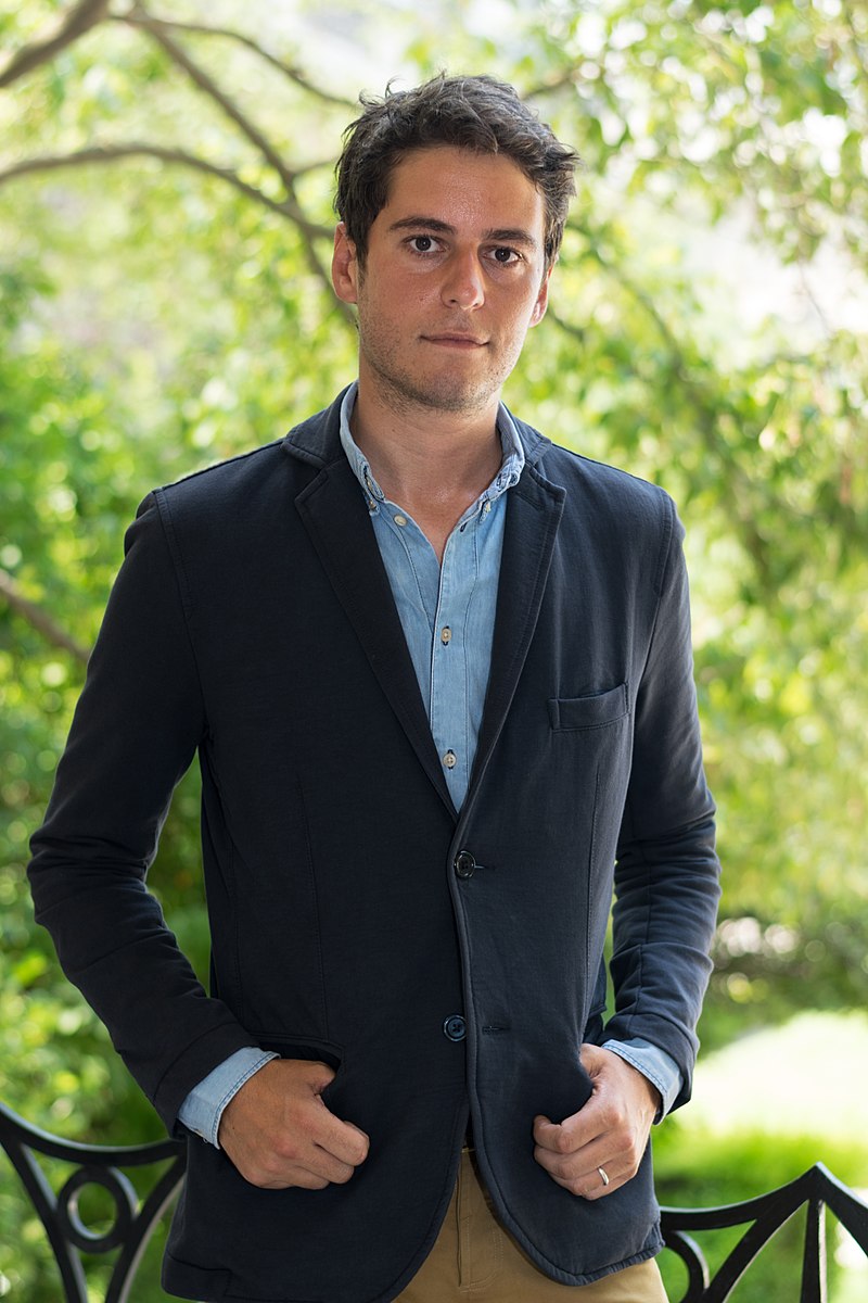 A photo of Gabriel Attal in Paris with a garden background while wearing a blue blazer.