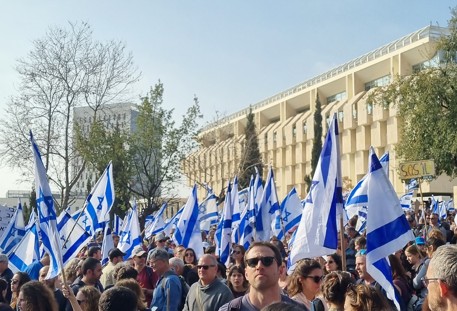 Israeli protestors congregating outside a building and waving Israeli flags.