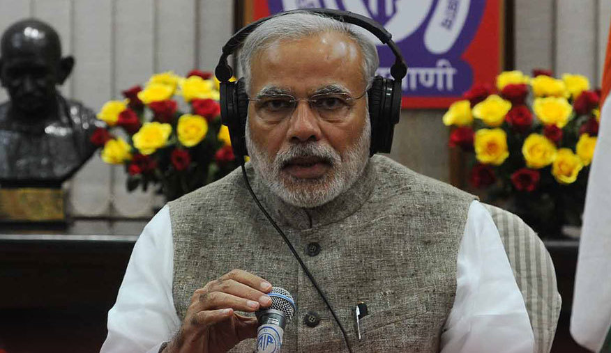Indian prime minister Narendra Modi sitting in front of a microphone, wearing headphones.