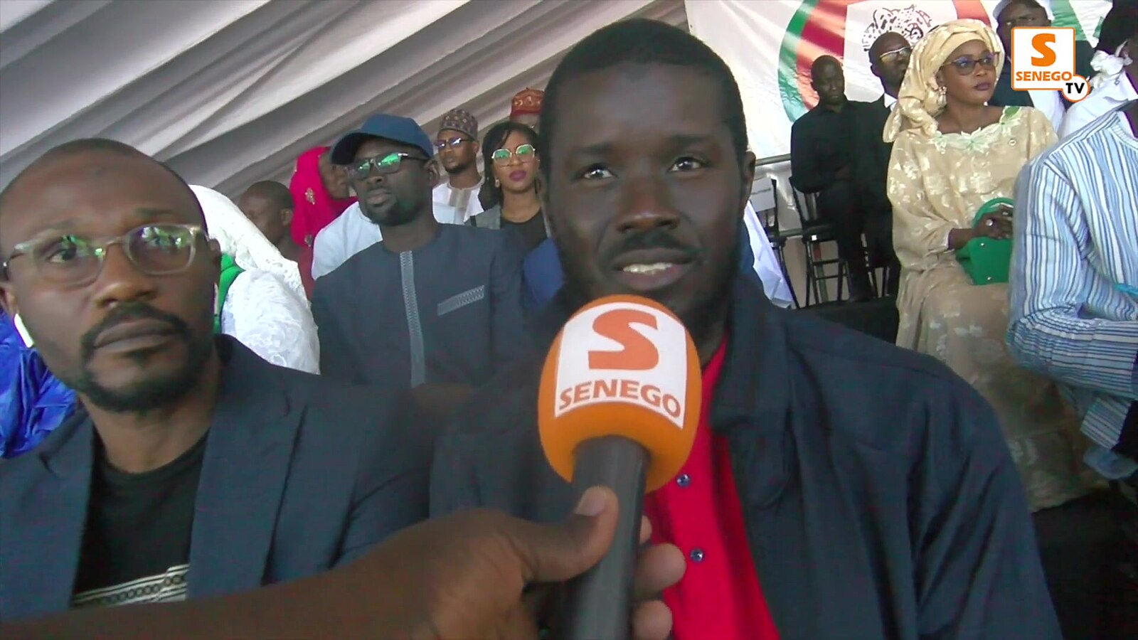 Bassirou Diomaye Faye speakiing into an orange mircrophone during a press conference with Senego TV.