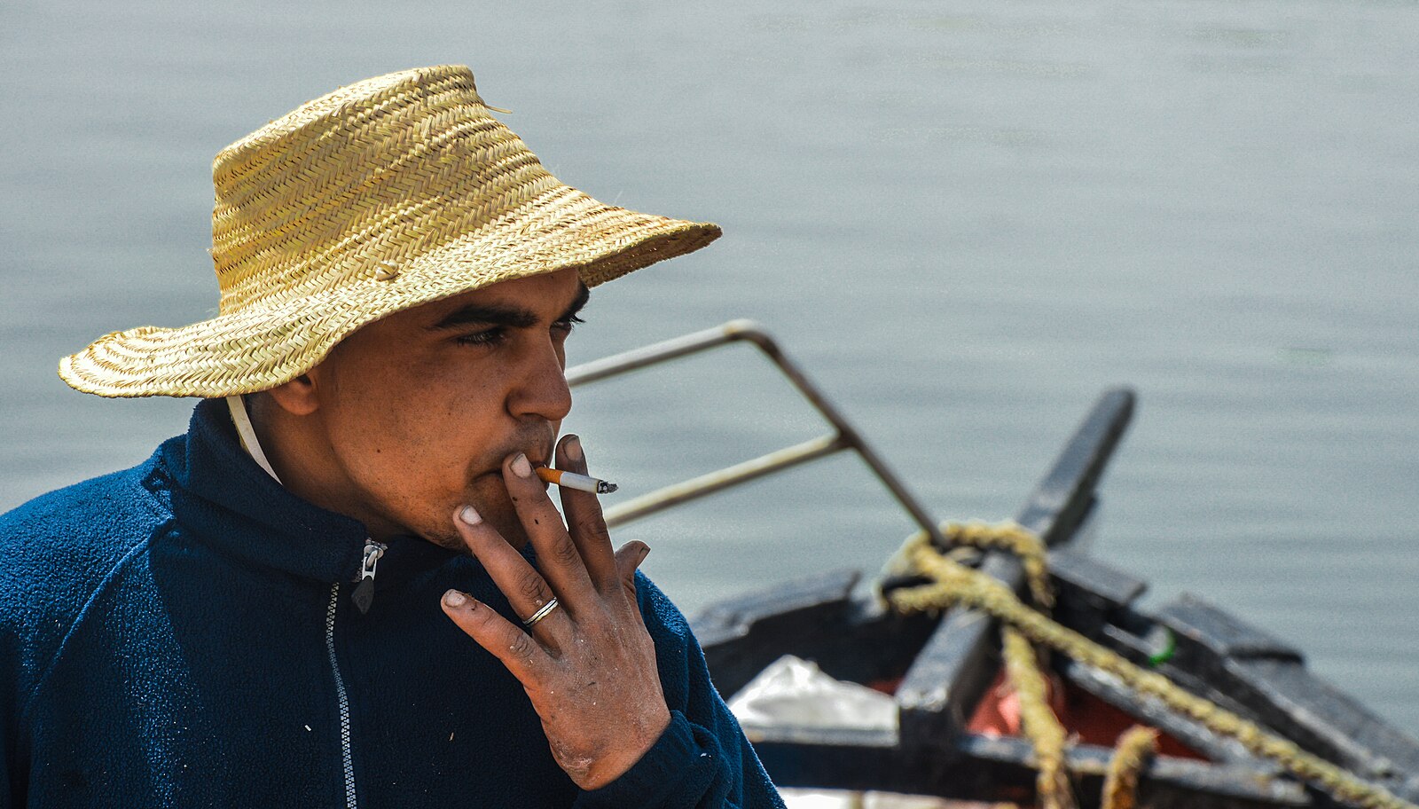 A Tunisian fisherman wearing a strawhat smoking while his boat is being refueled in Bizerte, Tunisia in 2016.