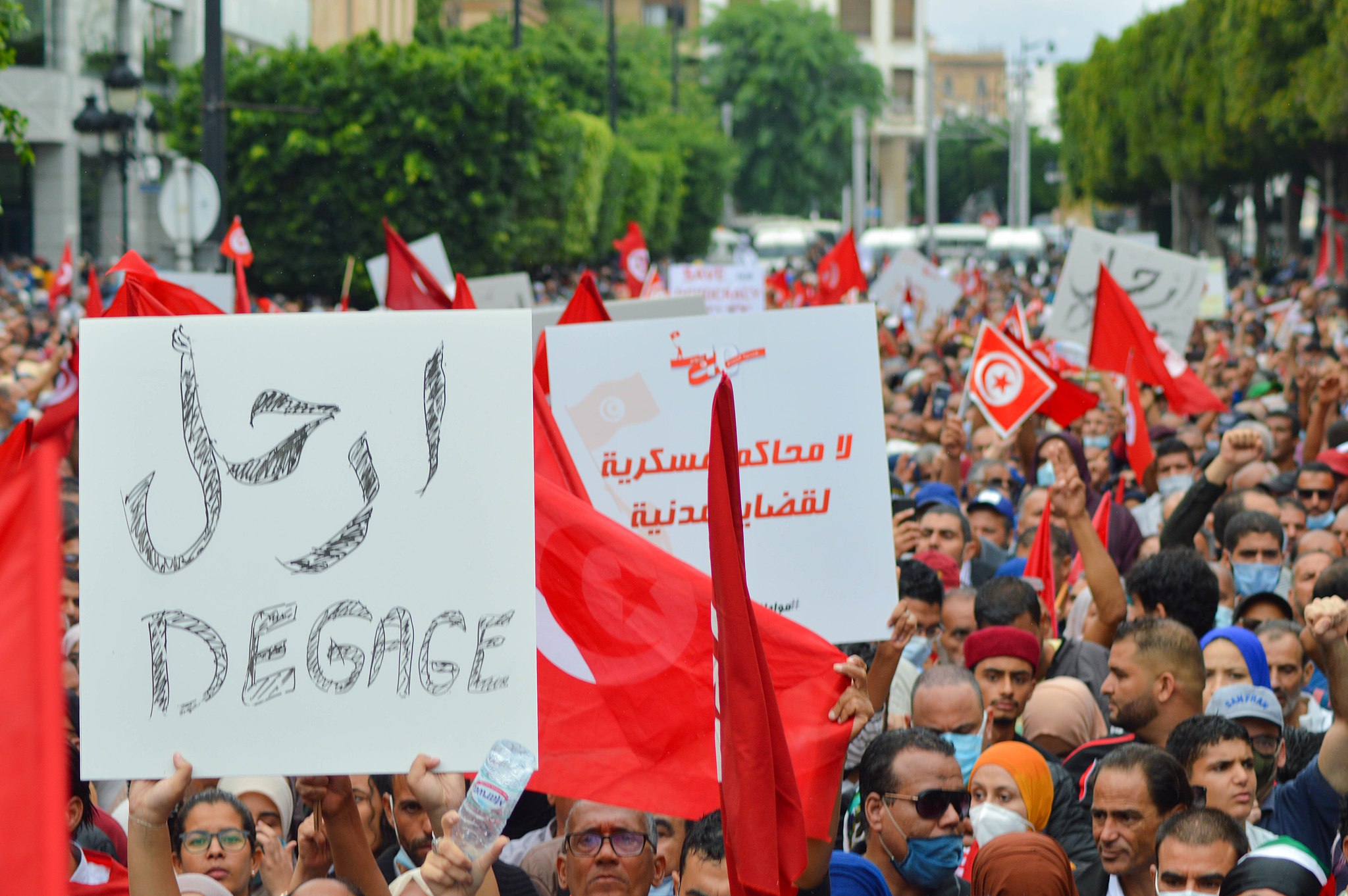 Tunisian protestors in 2021 protesting at a main square, as a group, while waving Tunisian flags