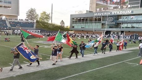 People waving flags from many different countries march around the football field at Dee Glen Smith Stadium.