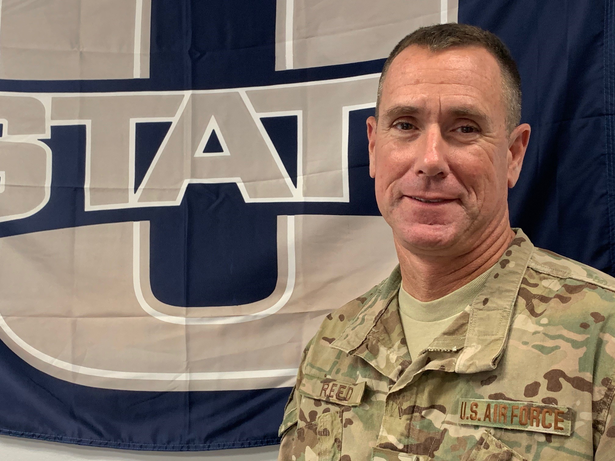 Col. Reed standing in front of a USU banner