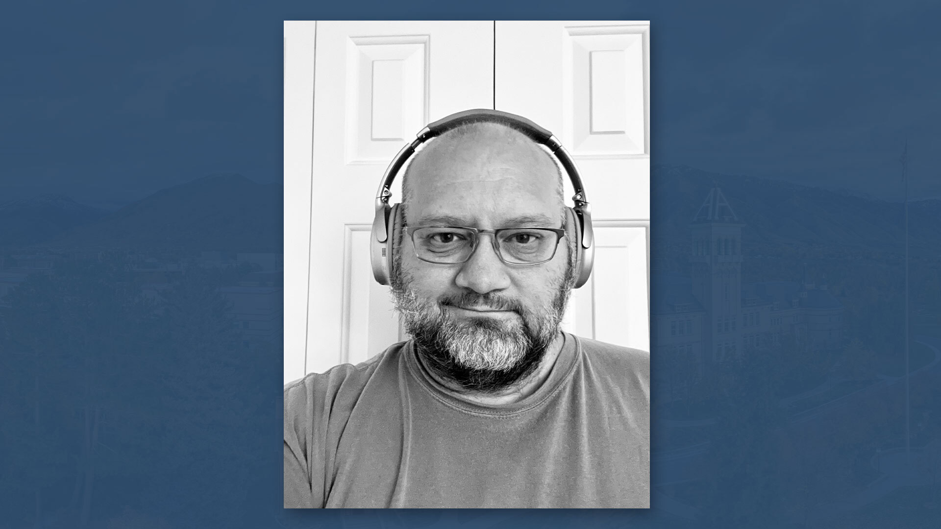 Black and white image of Professor Joshua Thoms wearing headphones on a blue background